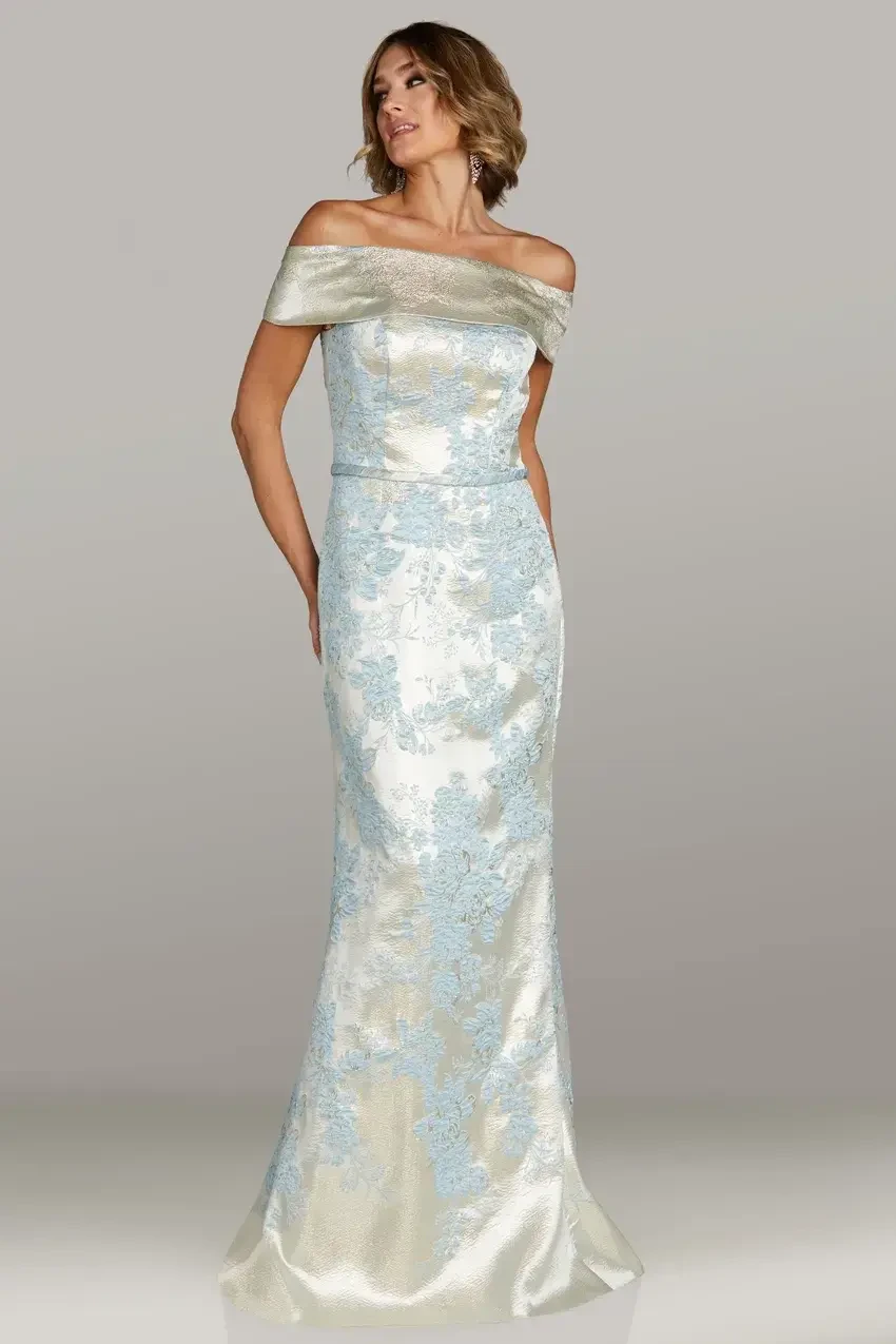 Model is wearing a fitted off-the-shoulder mermaid gown with a sweeping skirt and delicate belt accent.