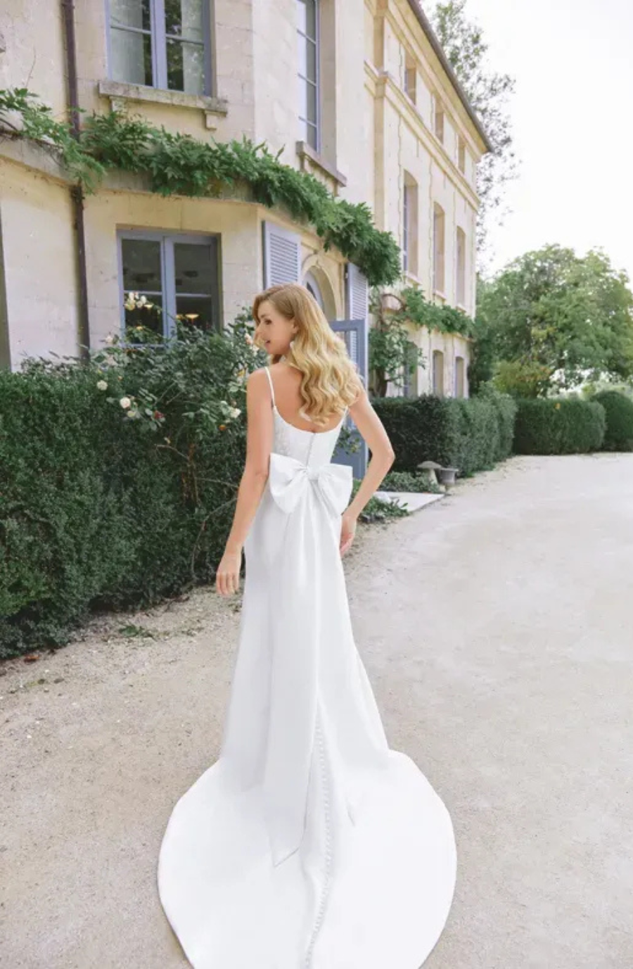model is wearing a sleeveless fit and flare wedding dress with a large bow on the back