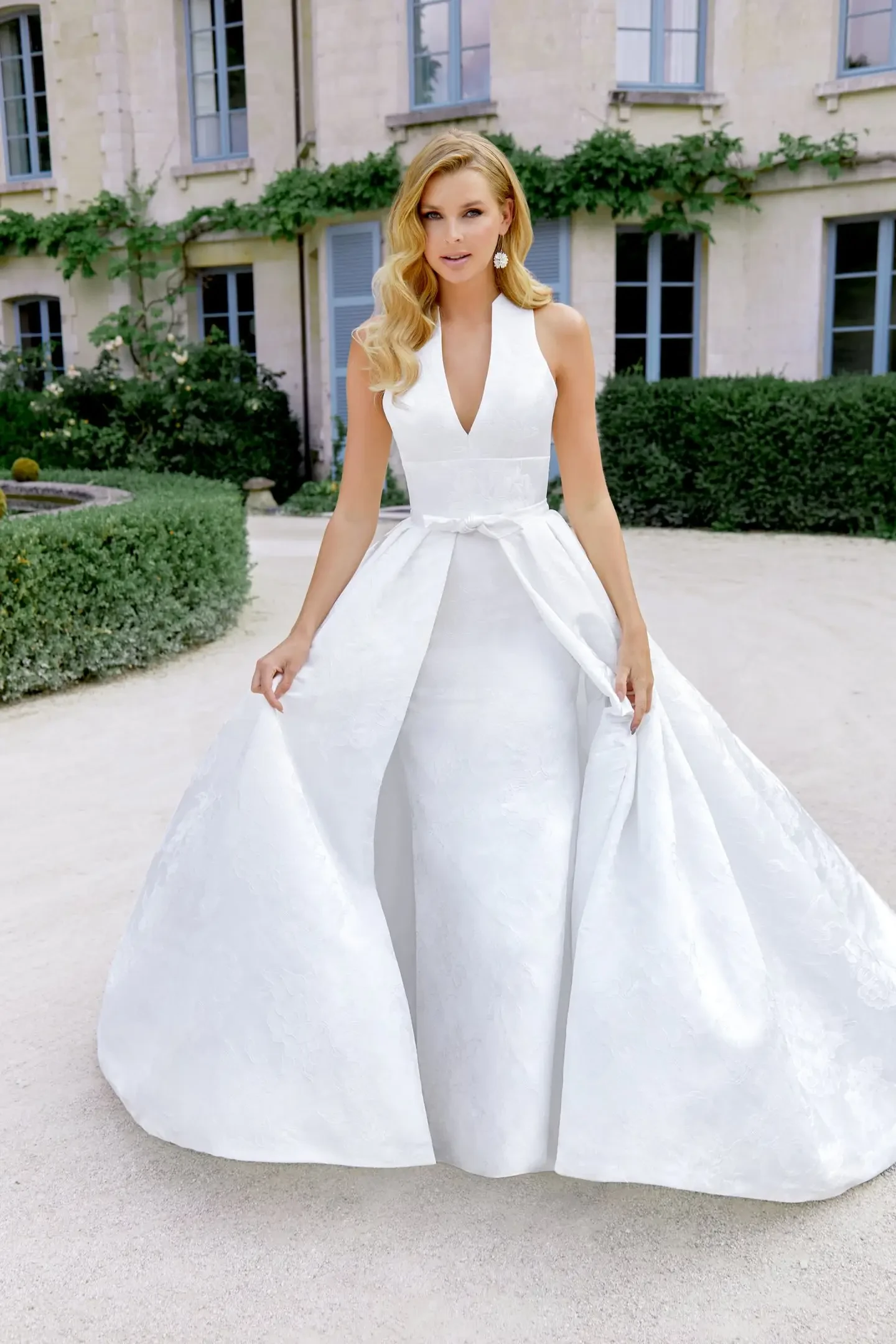 model is wearing a sleeveless wedding dress with an overskirt