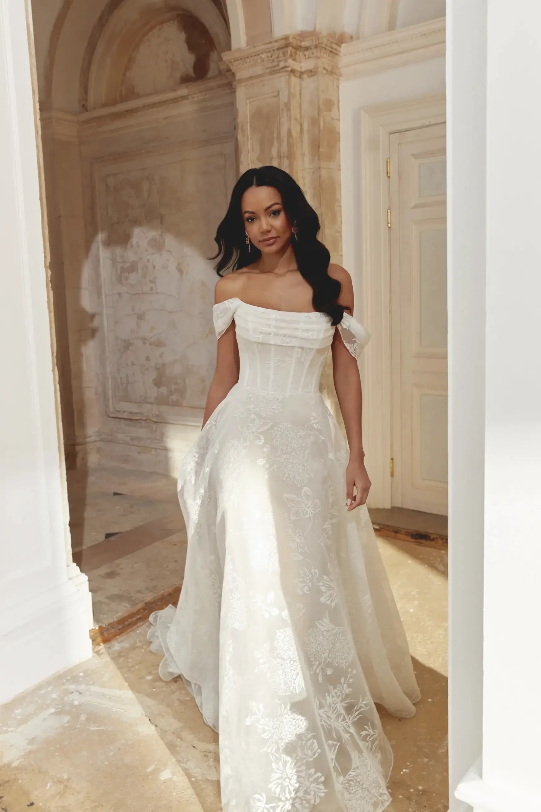 A woman is wearing an elegant white dress in a grand, light-filled indoor setting.