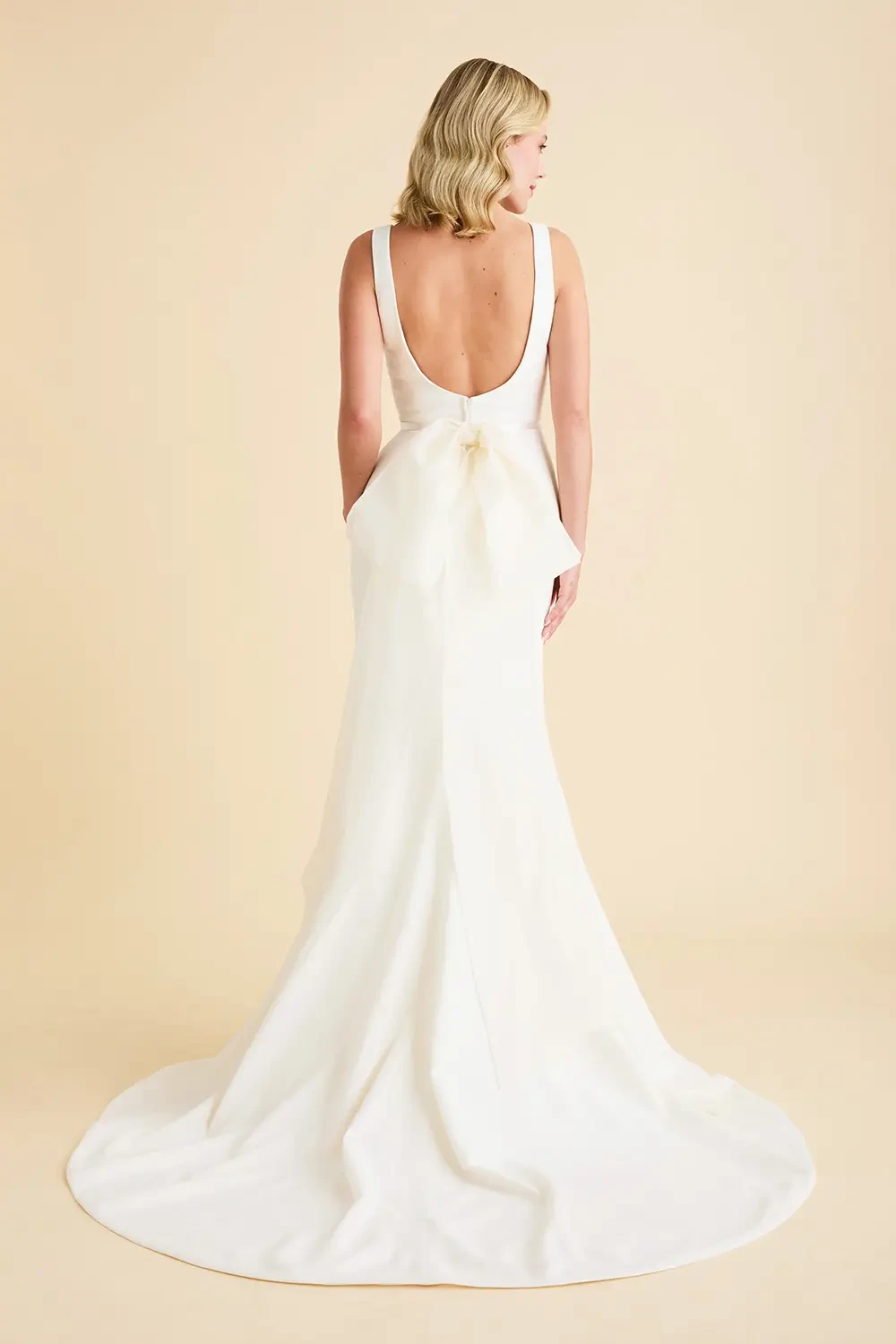 model is wearing a fit and flare wedding dress with an open back and bow on the back