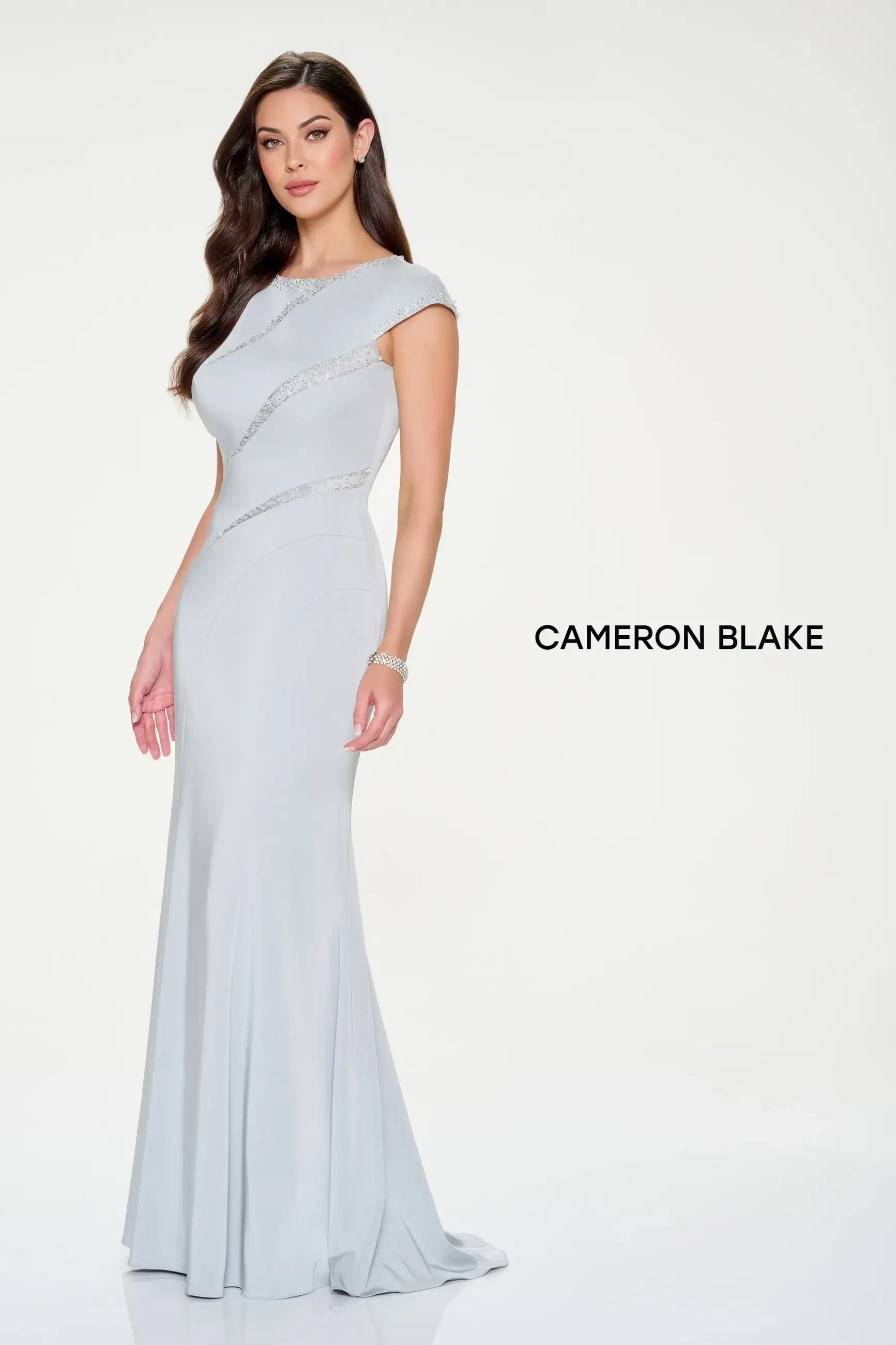 Model is wearing a crepe fit-and-flare gown with cap sleeves and asymmetric stone embellishments.