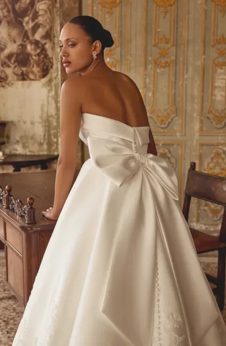 model is wearing a strapless ball gown wedding dress with a large bow on the back