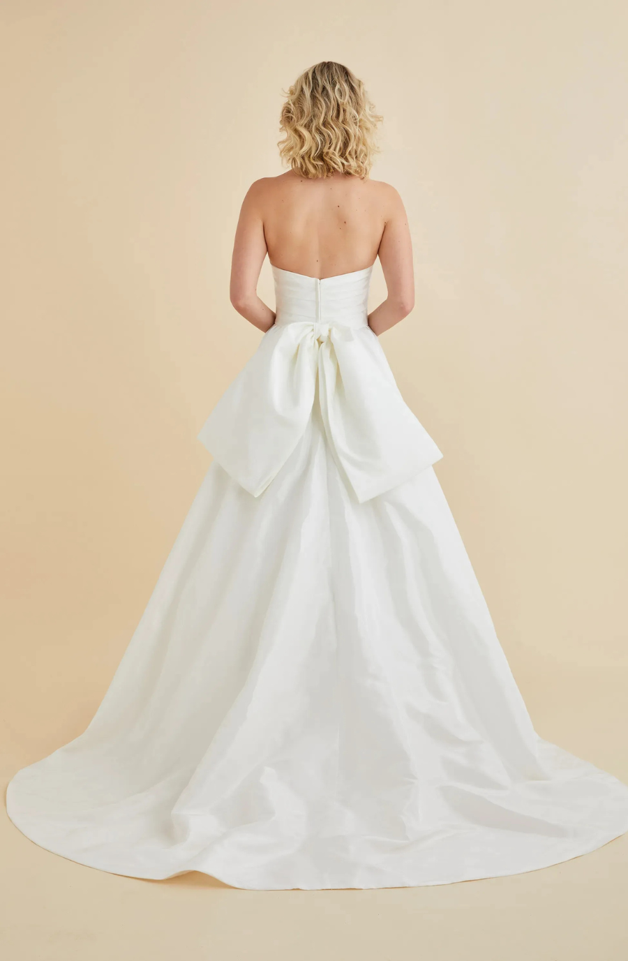model is wearing a strapless wedding dress with a large bow on the back